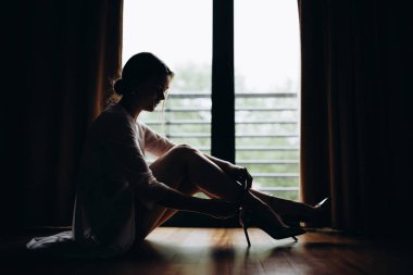 Çekici genç bir kadın yerde oturuyor ve şık yüksek topuklu ayakkabılar giyiyor.          