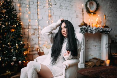 Genç ve seksi bir kadın, kumral saçlı rahat bir Noel arifesinde poz veriyor.           