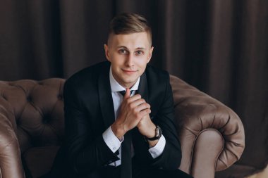 Takım elbiseli yakışıklı genç damat portresi oturuyor ve kameraya gülümsüyor.  