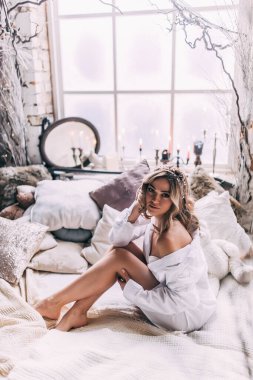 Beyaz gömlekli çekici genç bir kadın sabahları yatakta oturuyor.