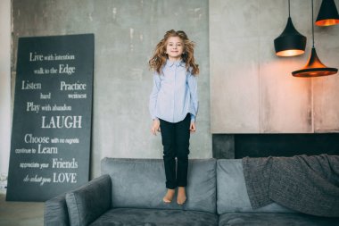 Küçük kız stüdyoda kanepede zıplıyor. 