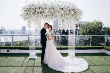 Gelin ve damat düğün günlerinde çiçek kemerinin yanında poz veriyorlar.