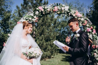 Güzel, mutlu gelin ve damat, düğün günlerinde çiçek kemerinin yanında.    