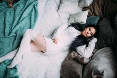 Güzel, genç, esmer bir kadın, rahat bir şekilde yatakta uzanıyor.                       