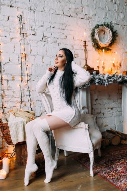 Genç ve seksi bir kadın, kumral saçlı rahat bir Noel arifesinde poz veriyor.           