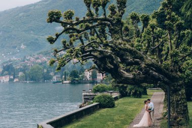 Gelin ve damat bir arada durur ve dağ gölünün kenarında sarılırlar.