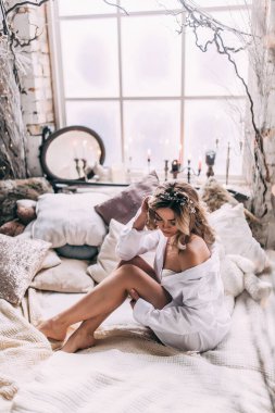 Beyaz gömlekli güzel sarışın kadın rahat bir odada yatakta poz veriyor. 