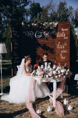 Güzel, mutlu gelin ve damat açık hava düğün töreninde ellerinde mumlar ve çiçeklerle masada oturuyorlar..              