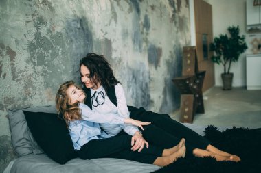 Stüdyo odasında yatakta poz veren genç mutlu anne ve kız. 