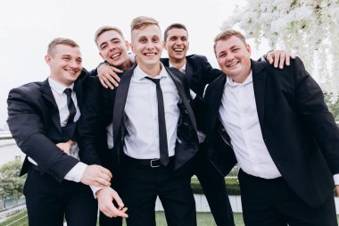 Bir grup mutlu genç adam ve damat düğün partisinde poz veriyorlar.       