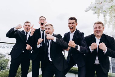 Bir grup mutlu genç adam ve damat düğün partisinde poz veriyorlar.       