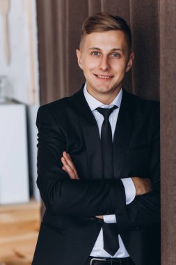 Takım elbiseli yakışıklı genç adam kollarını kavuşturup kameraya gülümsüyor.