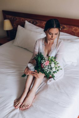 Bir buket çiçekli genç gelin sabahları yatağında oturuyor.    