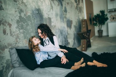 Stüdyo odasında yatakta poz veren genç mutlu anne ve kız. 