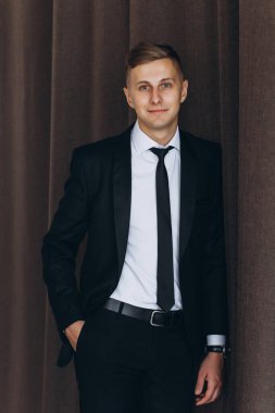 Siyah takım elbiseli ve kravatlı, kameraya gülümseyen yakışıklı bir gencin portresi.