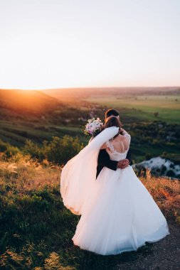 Mutlu gelin ve damat gün batımında güzel bir manzarada yürüyorlar.                