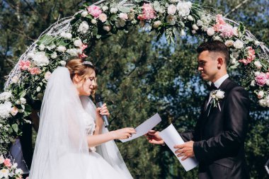 Güzel, mutlu gelin ve damat, düğün günlerinde çiçek kemerinin yanında.    