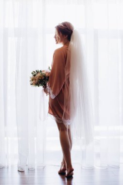 Pembe ipek bornoz ve duvak içinde güzel bir gelin Sabah düğün buketi tutuyor            