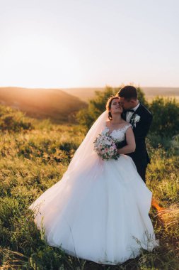 Mutlu gelin ve damat gün batımında güzel bir manzarada yürüyorlar.                