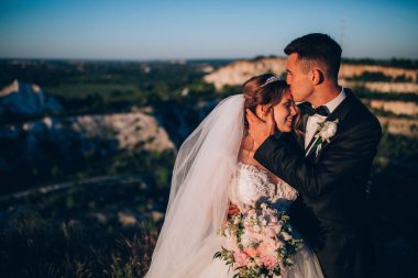 Mutlu gelin ve damat gün batımında güzel bir manzarada yürüyorlar.                