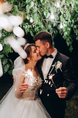 Mutlu genç gelin ve damat geceleri parkta maytapları öpüyor ve tutuyorlar.