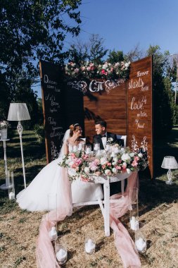 Güzel, mutlu gelin ve damat açık hava düğün töreninde ellerinde mumlar ve çiçeklerle masada oturuyorlar..              