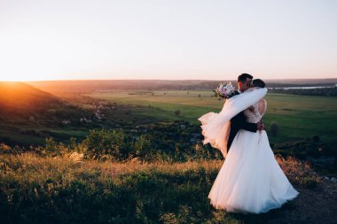Mutlu gelin ve damat gün batımında güzel bir manzarada yürüyorlar.                