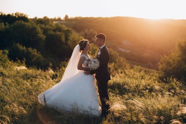 Mutlu gelin ve damat gün batımında güzel bir manzarada yürüyorlar.                