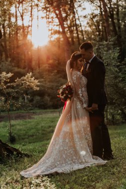 Güzel mutlu gelin ve damat doğada gün batımında poz veriyor.                