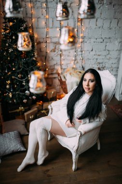 Genç ve seksi bir kadın, kumral saçlı rahat bir Noel arifesinde poz veriyor.           