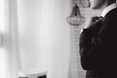 Siyah takım elbiseli damadın kravat taktığı siyah beyaz görüntü