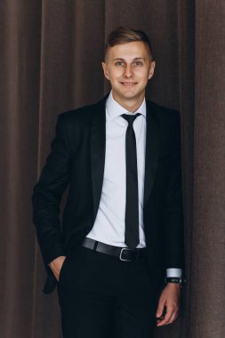 Siyah takım elbiseli ve kravatlı, kameraya gülümseyen yakışıklı bir gencin portresi.