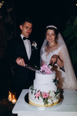 Mutlu gelin ve damat bir masada düğün pastası kesiyor.. 