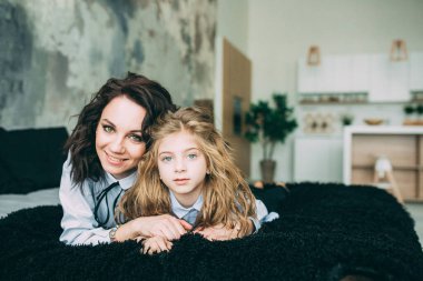 Stüdyo odasında yatakta poz veren genç mutlu anne ve kız. 