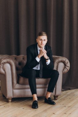 Şık takım elbiseli yakışıklı bir gencin portresi koltukta oturuyor.