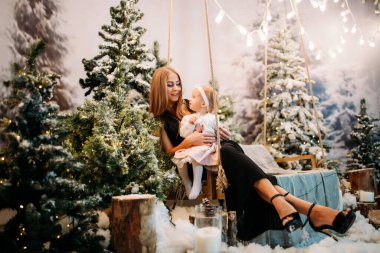 Güzel genç bir kadın bebeğiyle salıncakta poz veriyor. 