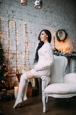 Genç ve seksi bir kadın, kumral saçlı rahat bir Noel arifesinde poz veriyor.           