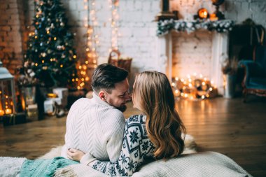 Genç ve güzel bir çift, bir şöminenin yanında çelenklerle süslenmiş bir odada oturuyor.