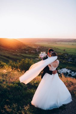 Mutlu gelin ve damat gün batımında güzel bir manzarada yürüyorlar.                