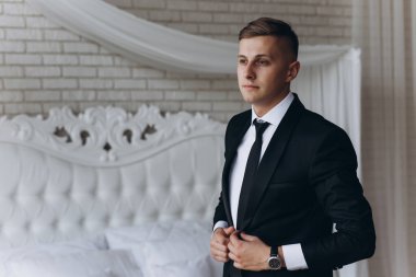 Genç damat sabah yatak odasında şık bir takım elbise giyiyor. 