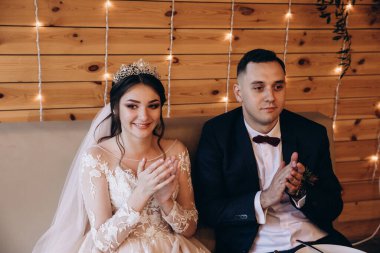 Mutlu evlilik çifti düğün resepsiyonunda oturup alkışlıyor.