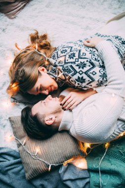 Genç ve güzel bir çift, bir şöminenin yanında çelenklerle süslenmiş bir odada oturuyor.