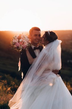 Güzel mutlu gelin ve damat doğada gün batımında poz veriyor.                