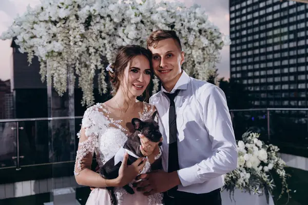 Terasta köpeğe poz veren genç bir çift. 