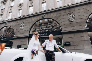 Güzel genç bir çift gelin ve damat şehirde beyaz düğün arabasının yanında poz veriyorlar.