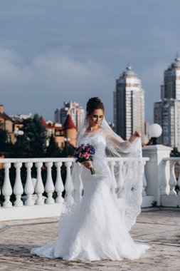 Şehirde poz veren zarif beyaz gelinlik içindeki güzel genç gelinin portresi.          