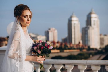 Şehirde poz veren zarif beyaz gelinlik içindeki güzel genç gelinin portresi.          