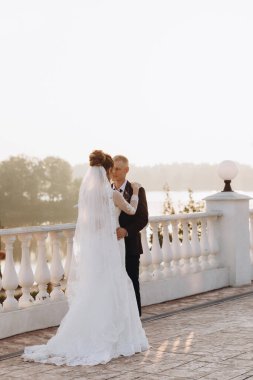 Güzel, genç, mutlu gelin ve damat düğün günü nehir kenarında poz veriyor.               