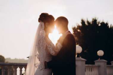 Güzel mutlu gelin ve damat düğün gününde gün batımında dışarıda poz veriyorlar.                 