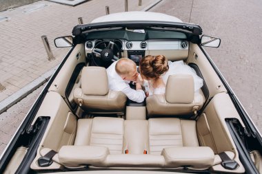 Güzel genç bir çift gelin ve damat şehirde arabada poz veriyorlar.